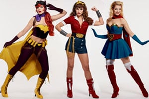 Three women dressed as superheroes posing for a photo with children's sewing patterns.